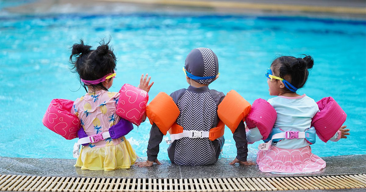 Family Water Safety at Pool Canadian family practicing water safety at pool with children wearing bright colored swimsuits and life jackets