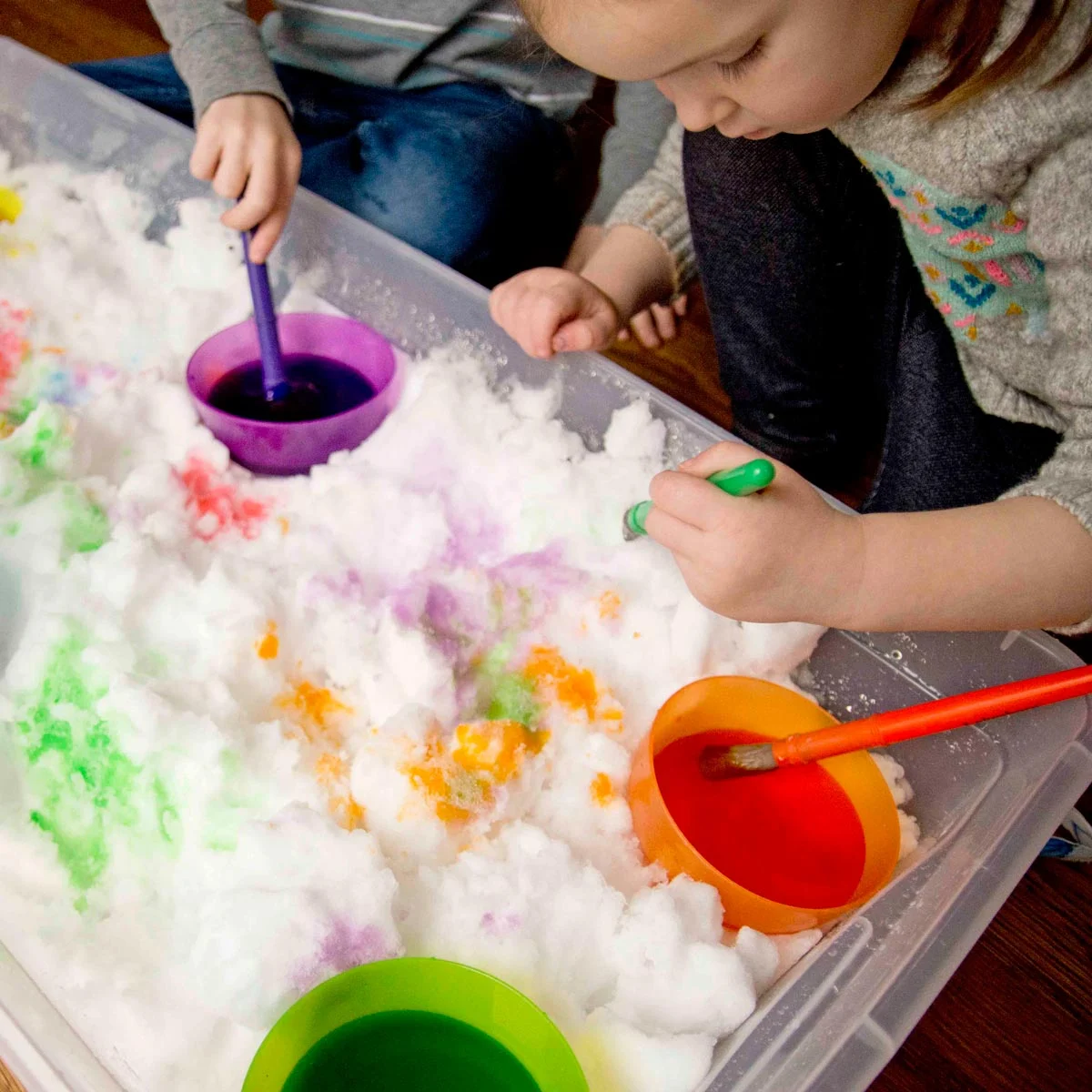 Toddler exploring a winter sensory bin with snow paint indoors