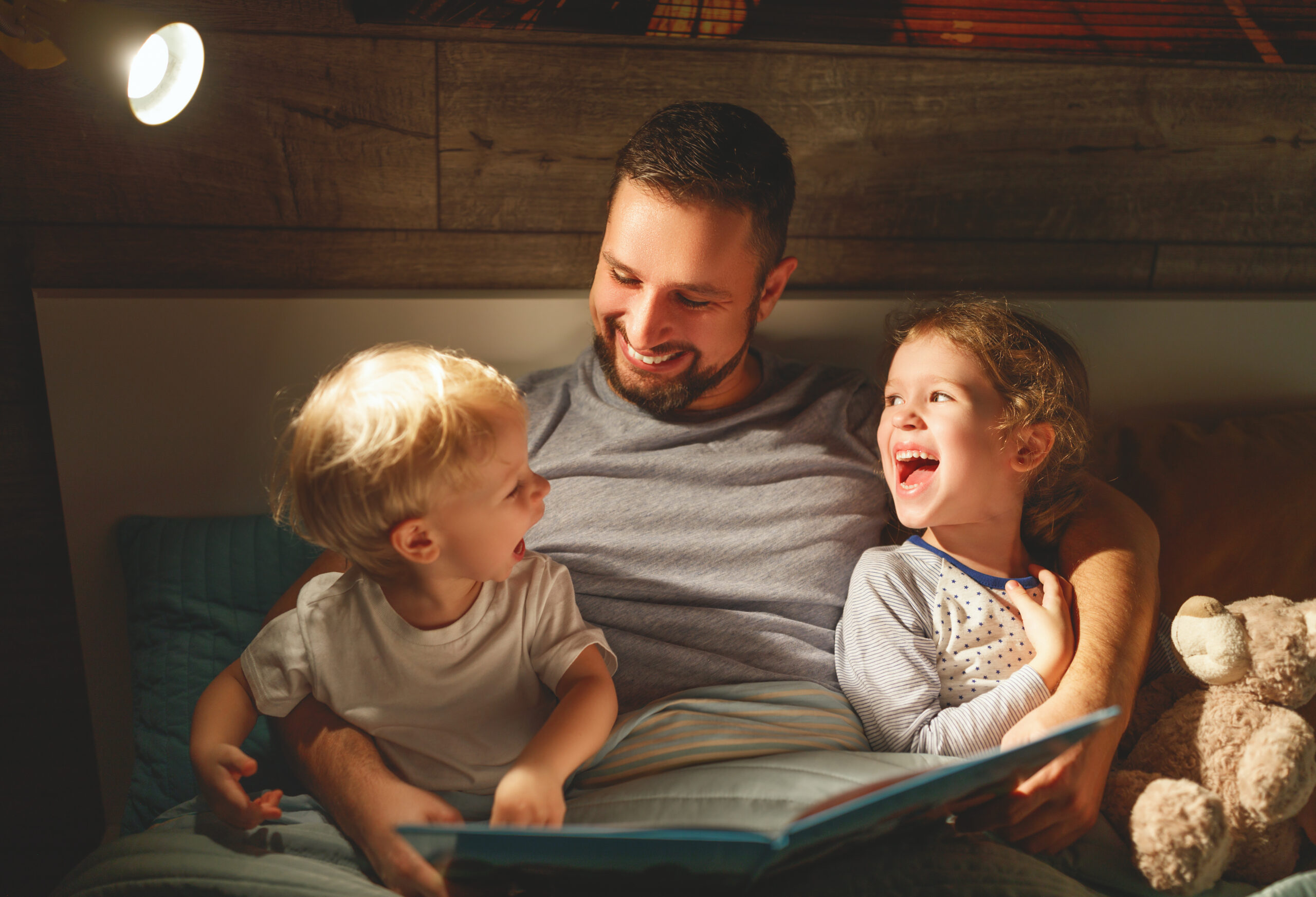 Parent reading at bedtime with a toddler while caring for a newborn nearby